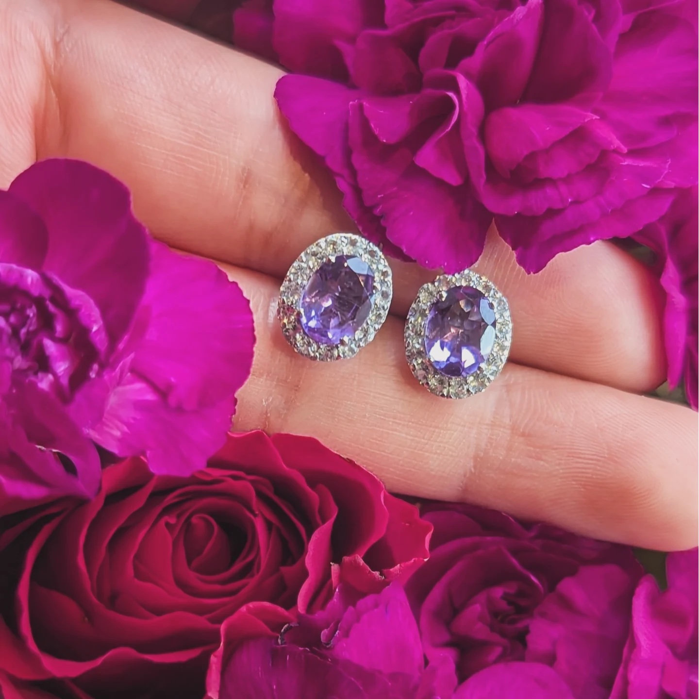 Amethyst earrings with white topaz held among pink and red flowers.