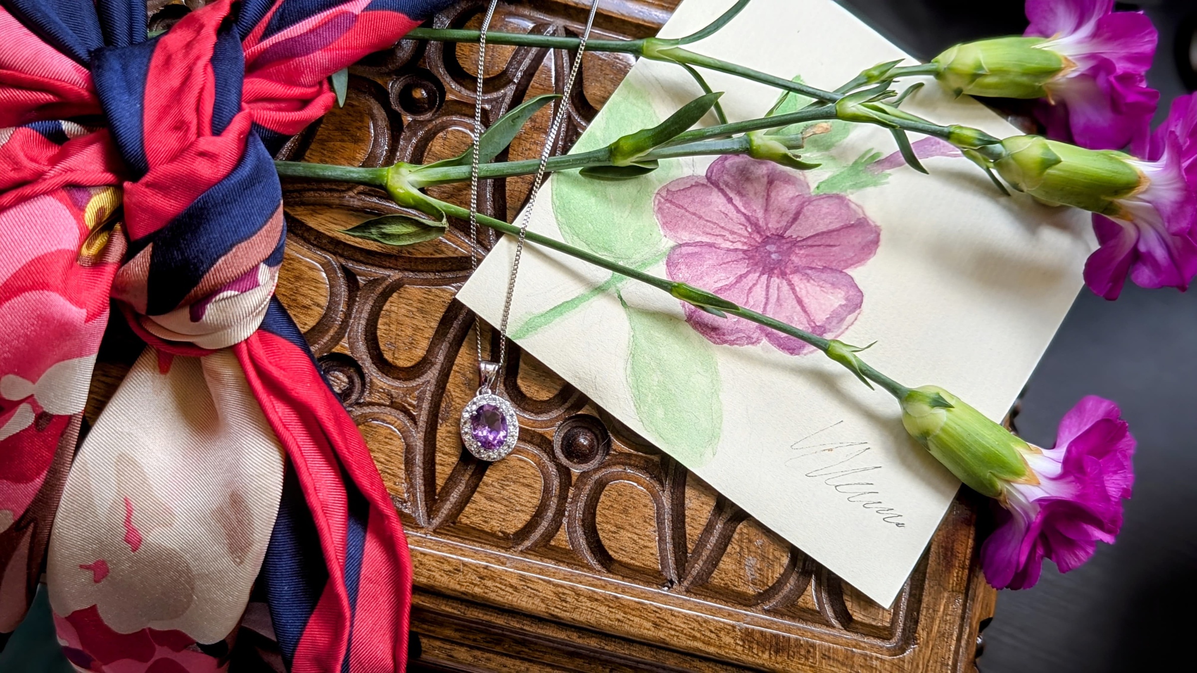 Amethyst pendant styled with flowers, a silk scarf and a painted card.