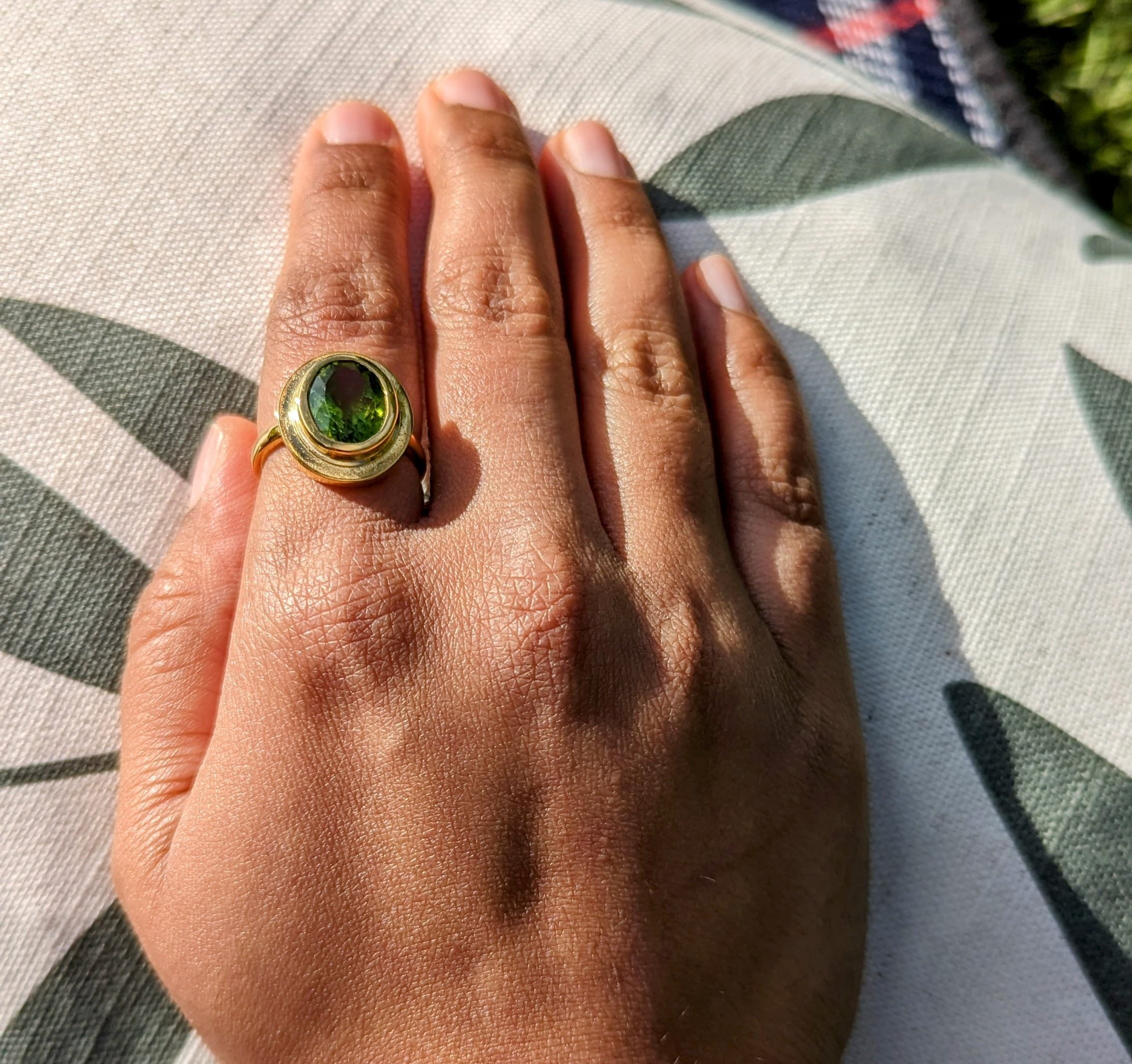 Peridot ring worn in sunlight on a patterned cushion.