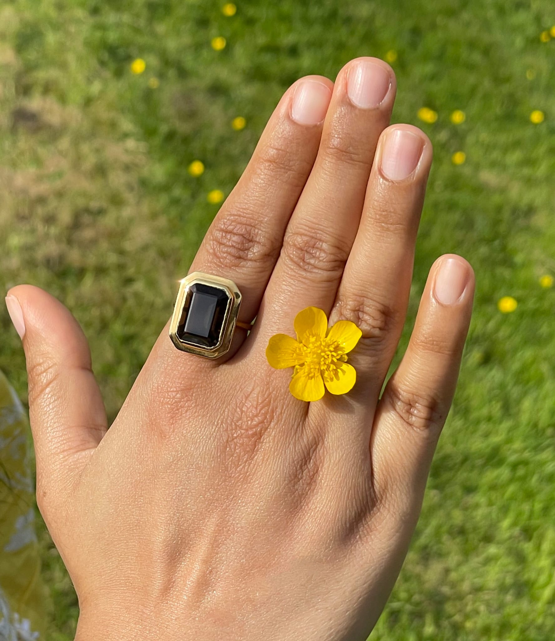 Smoky quartz ring worn in natural light with a yellow flower.