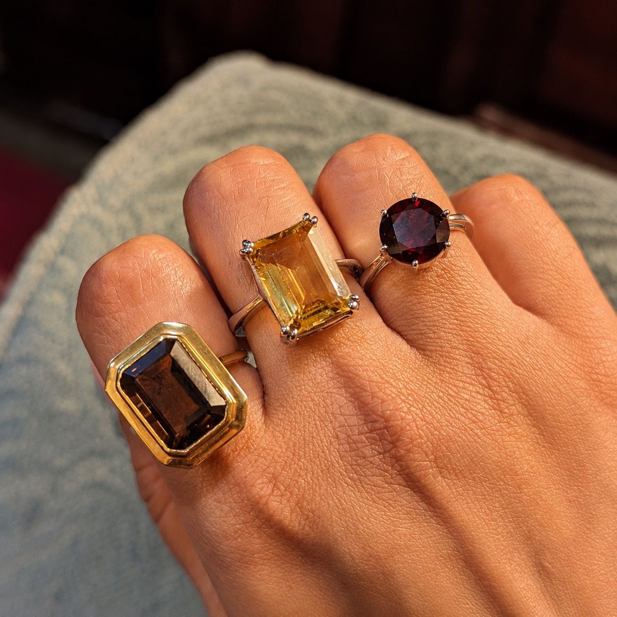 Smoky quartz, citrine and garnet rings worn on a hand in warm light.